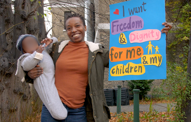 A woman holding a poster that says 'I want dignity and freedom for me and my children'. In her other hand, she is holding her baby - both are smiling.